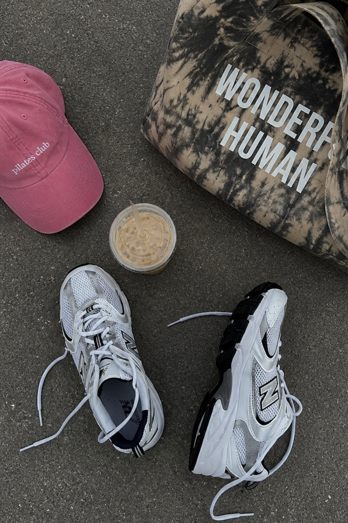 Two sneakers, a pink cap, a black and white cap with 'Wonder Human' text, and a small container on a concrete surface.