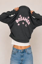 Person wearing a anthracite sweatshirt with 'Dreamer' printed on it, standing against a plain background.